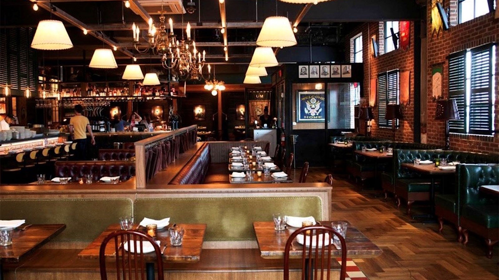 The St. Anselm dining room with brick walls, hanging light fixtures and chandeliers, and wooden chairs and wood-cloth benches